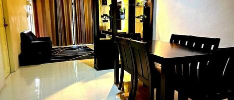 A dining area with a table and chairs, a cabinet with glass doors, and a window with curtains.