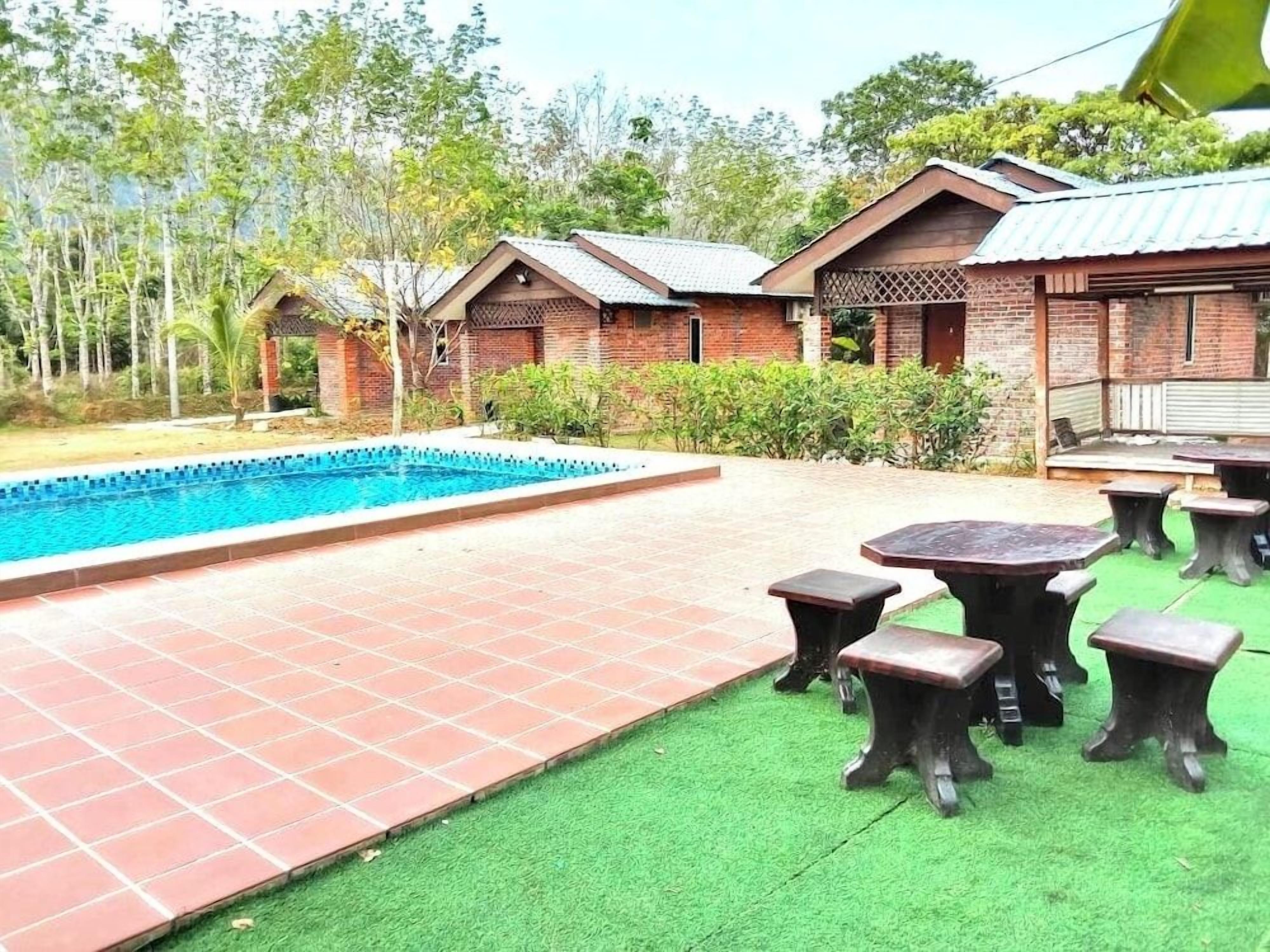 A pool area with a tiled deck and green artificial turf, surrounded by brick buildings with a covered patio.