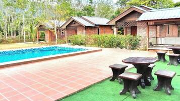 A pool area with a tiled deck and green artificial turf, surrounded by brick buildings with a covered patio.