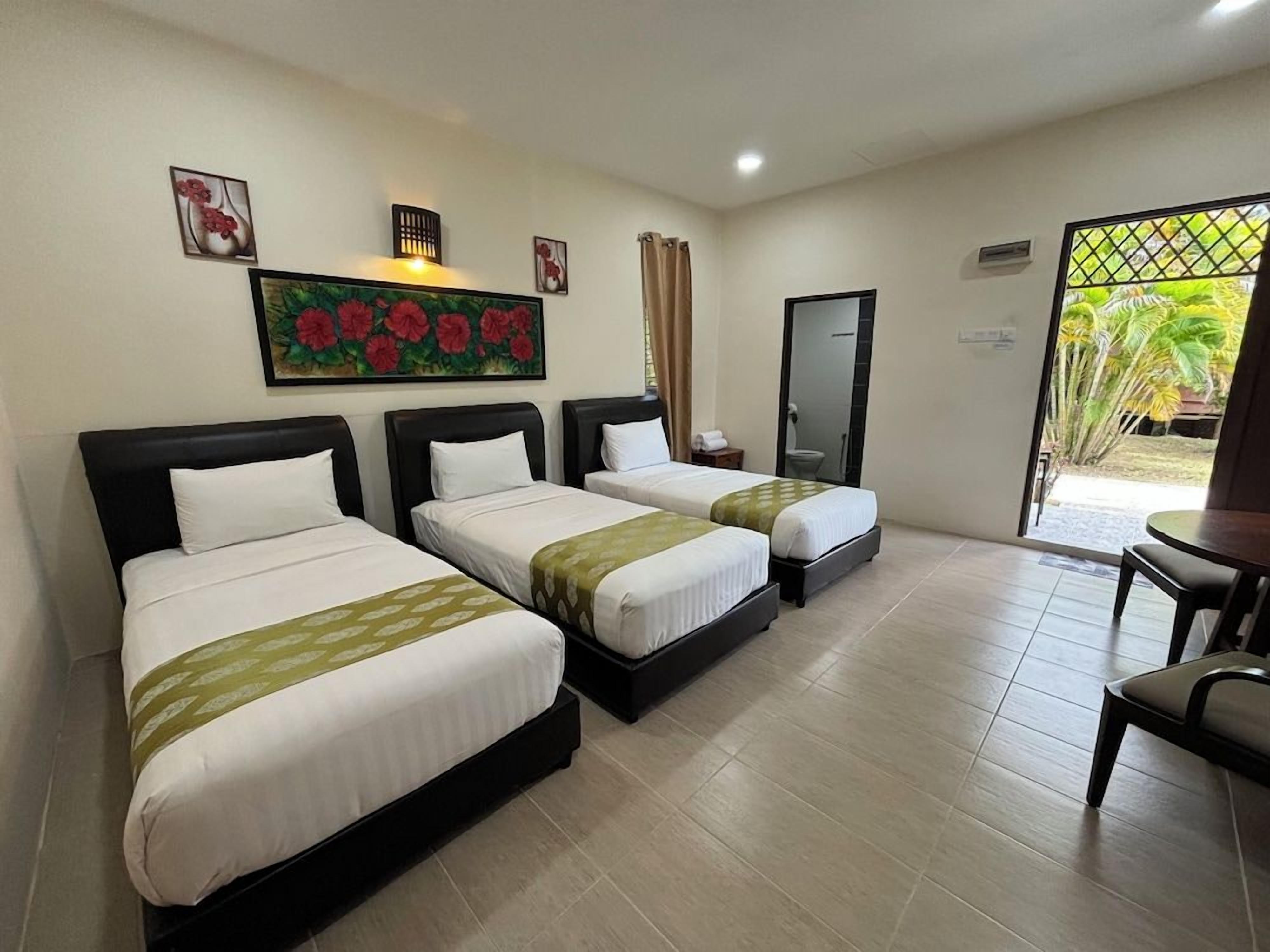 A hotel room with three beds, a desk, and a view of the outdoors.