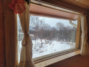 A window with curtains tied back, revealing a snowy landscape with trees and a building in the background. - Beautiful cabin located close to everything with (EU) King size mattress in upstairs loft, large jetted tub and views of Grewing Glacier and Kachemak Bay from the windows. (Homer)