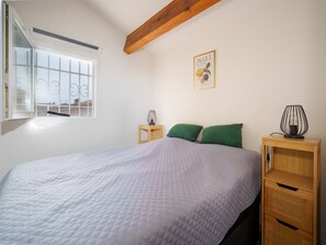 A bedroom with a bed, a window with bars, a bedside table with a lamp, a wall art piece, and a wooden nightstand. - Clos des Amandines Ndeg93 - 3P6 (Agde)