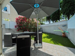An outdoor patio area with a table and chairs, a large umbrella, and a lawn. - Clos des Amandines Ndeg93 - 3P6 (Agde)