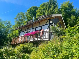 A traditional chalet with a balcony, surrounded by lush greenery.