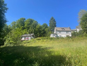 Ein traditionelles, zweistöckiges Haus mit Balkon, umgeben von üppigem Grün und Bäumen.