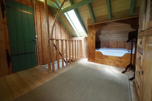 Un interior de madera con techo inclinado, una puerta verde, una cama con colchón blanco y un aparador de madera.