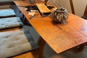 Una mesa de comedor de madera con un farol tejido y una silla de cuero encima.