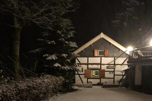 A snow-covered pathway leading to a traditional chalet-style building with a steep roof and wooden shutters.