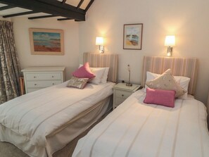 A hotel room with two beds, each with a pillow and a bedside table. There are two wall-mounted lamps and a painting on the wall. - Iveridge (Whitby)