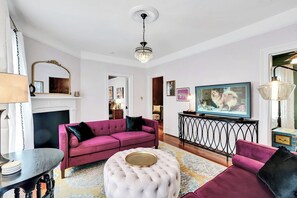 A living room with a pink sofa, a round ottoman, a television, and a chandelier. - Chic 2 Bedroom Flat in Historic District - Wilmington (Wilmington)