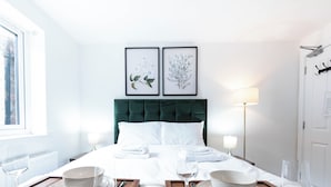 Ein Hotelzimmer mit einem Bett, zwei gerahmten floralen Kunstwerken, Nachttischlampen und einem Essbereich mit Tellern und Gläsern.