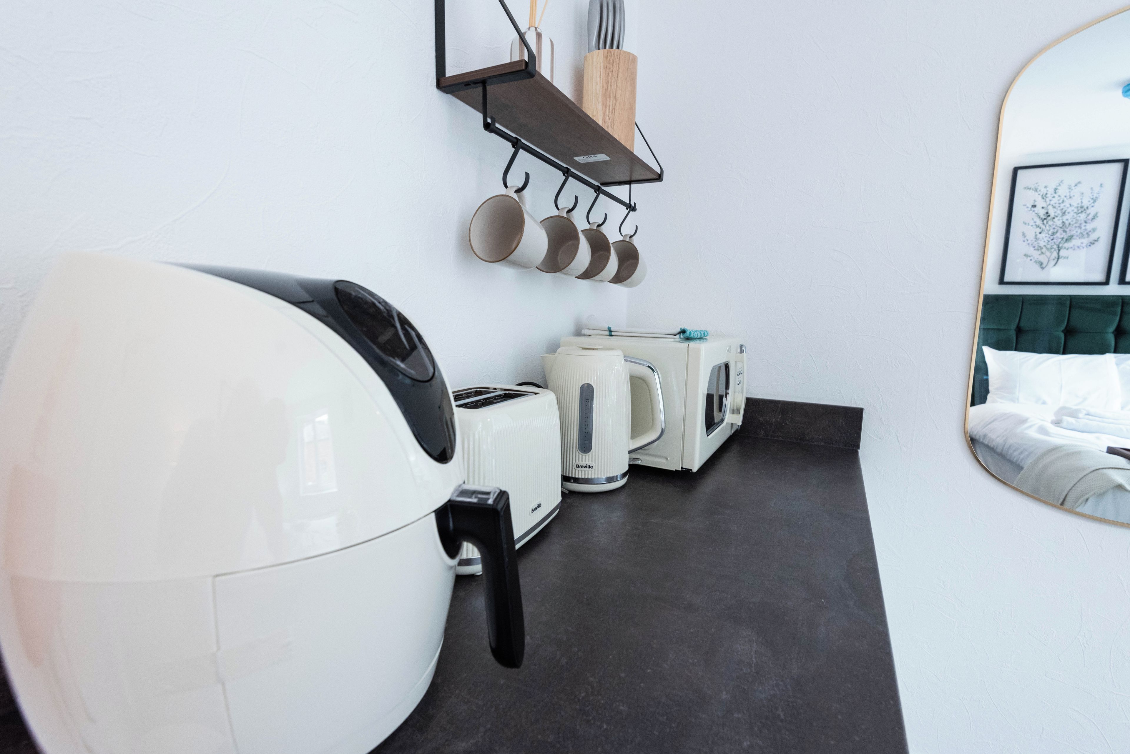 A kitchenette with a toaster, kettle, and hanging pots.