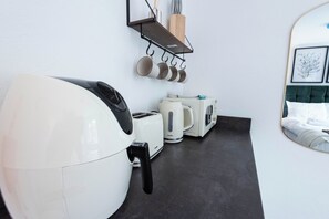 A kitchenette with a toaster, kettle, and hanging pots.