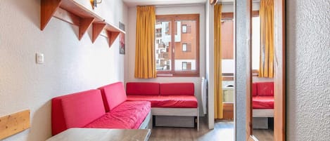 A compact room with a wooden table, red sofa, and a window with yellow curtains.