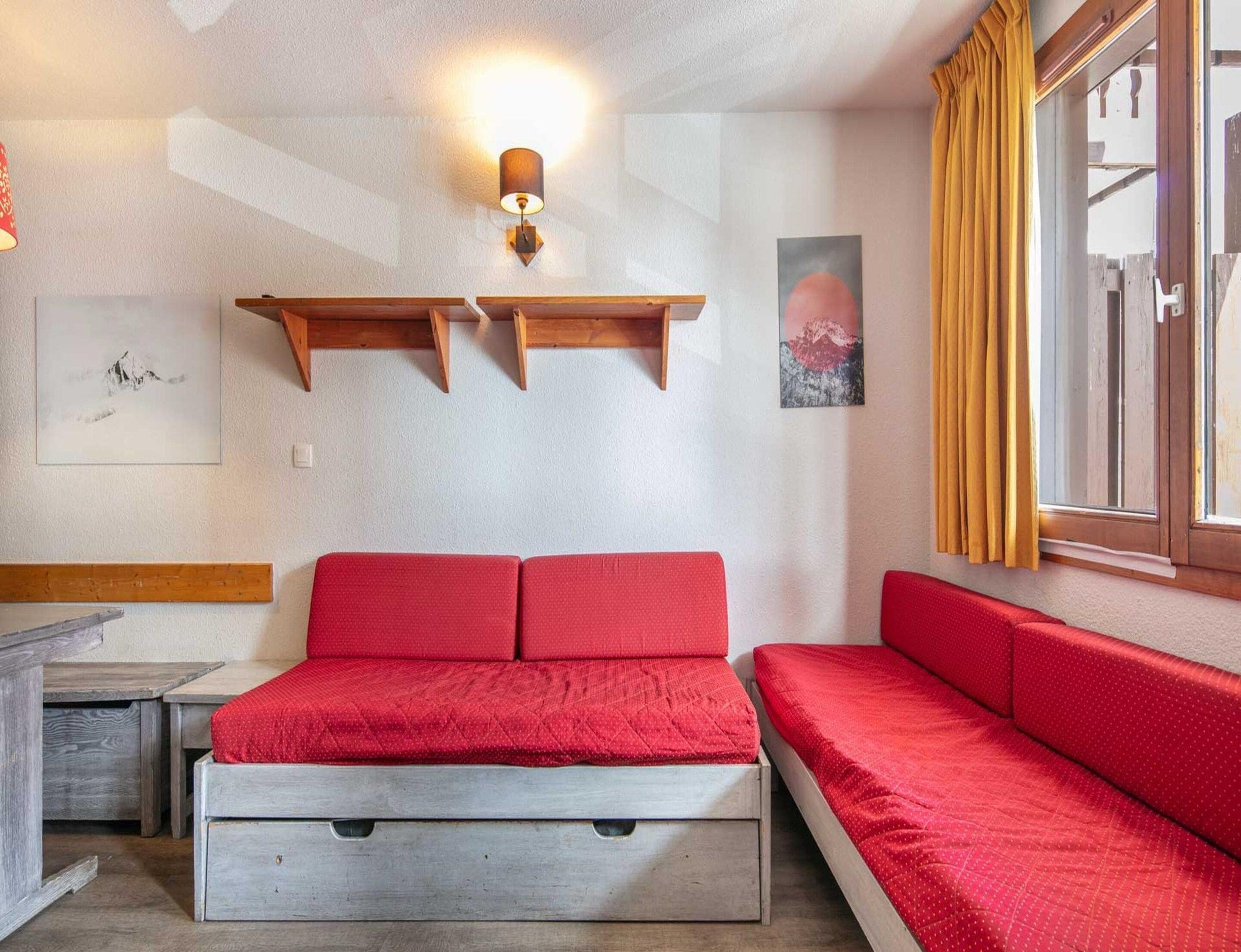 A bedroom with a bed, a bench, a wall-mounted shelf, and a window with curtains.