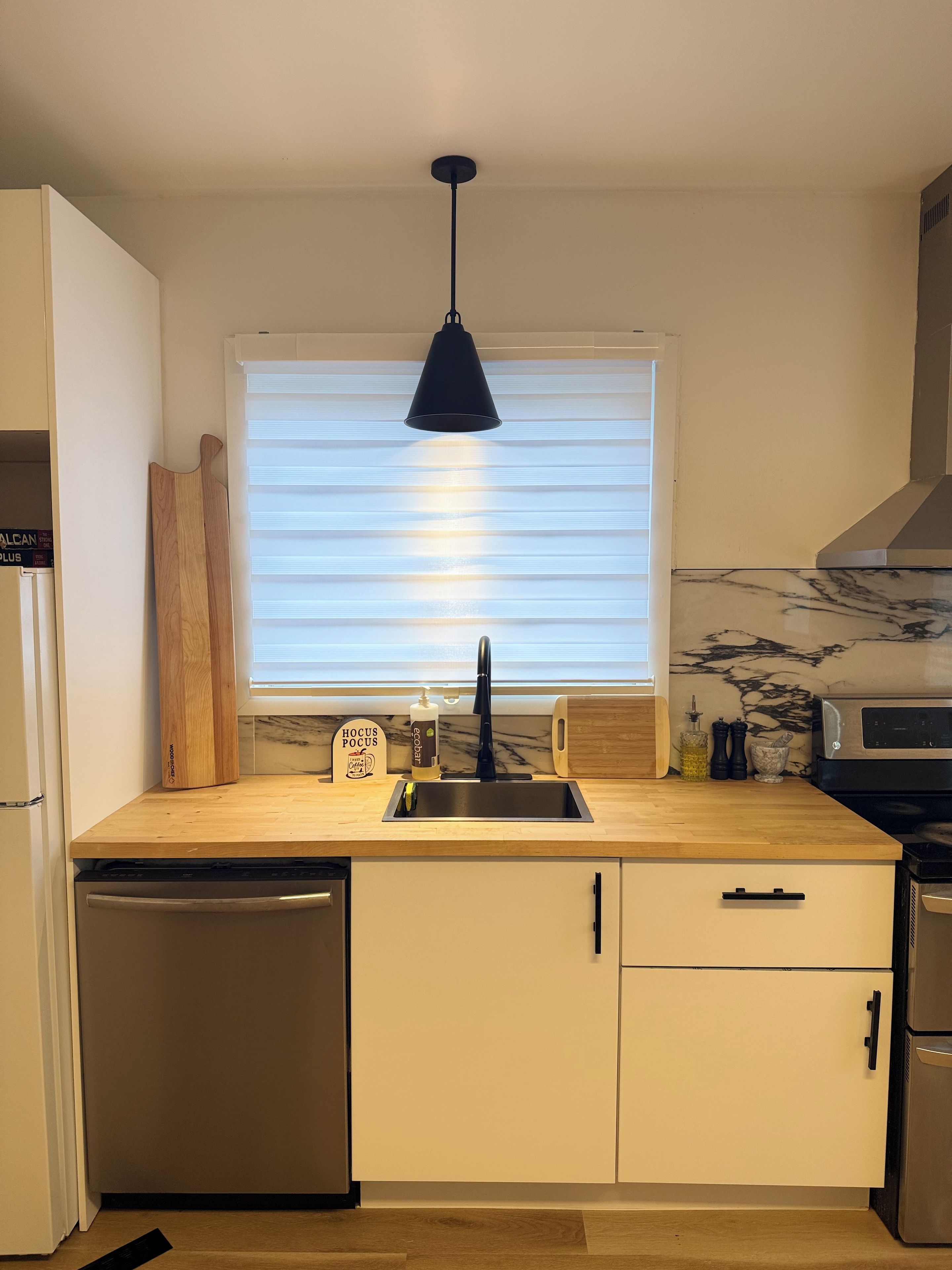 A kitchen with a black pendant light, a window with blinds, a sink, and a microwave.