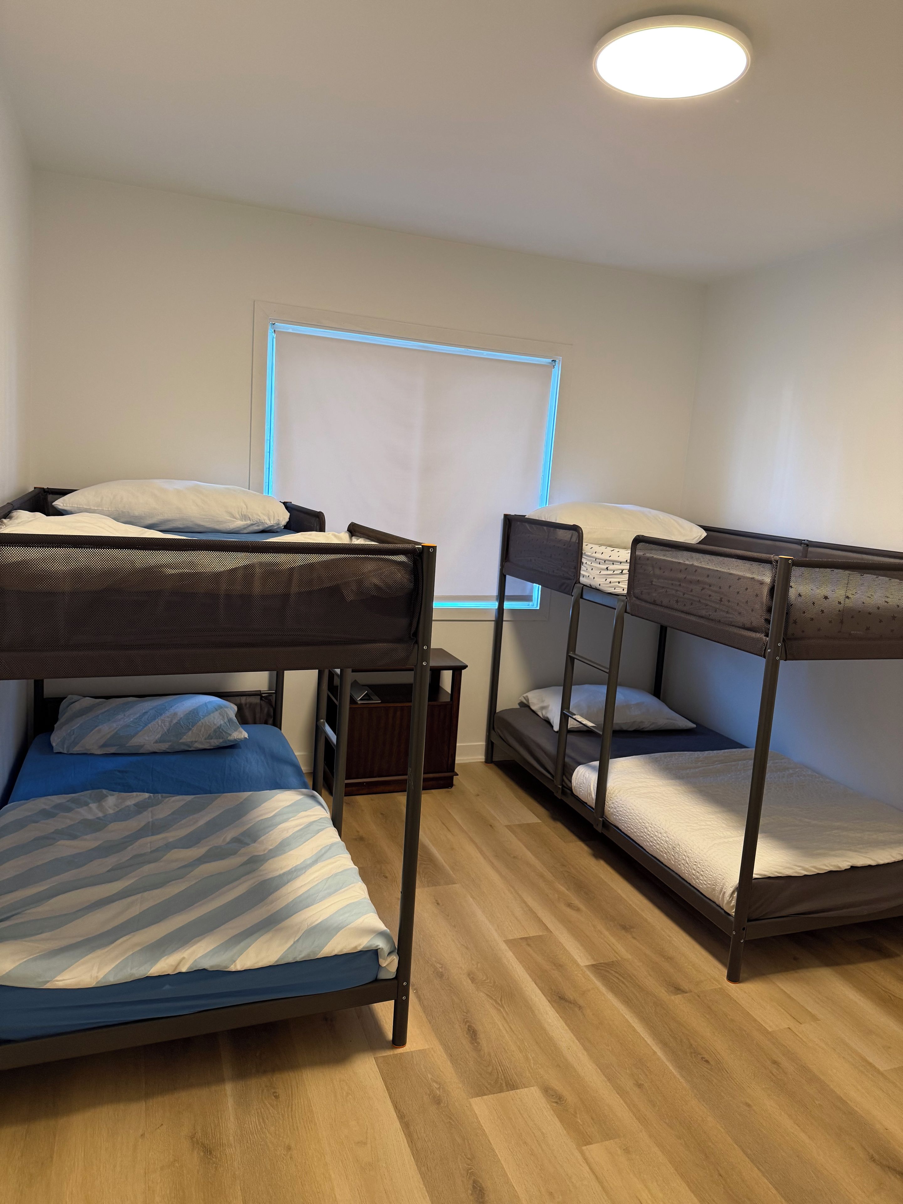 A room with bunk beds, a small table, and a window with blinds.
