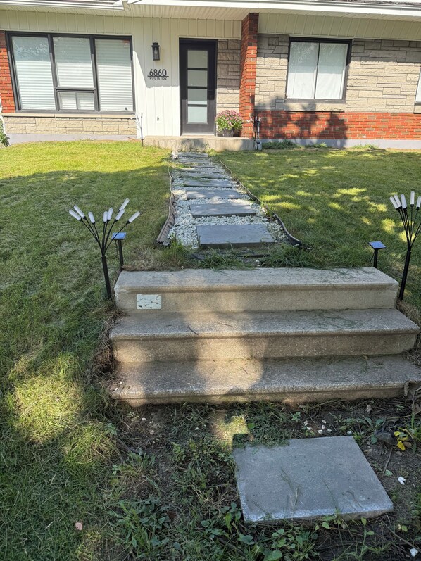 A residential property with a front yard, a driveway leading to a house, and a set of concrete steps.