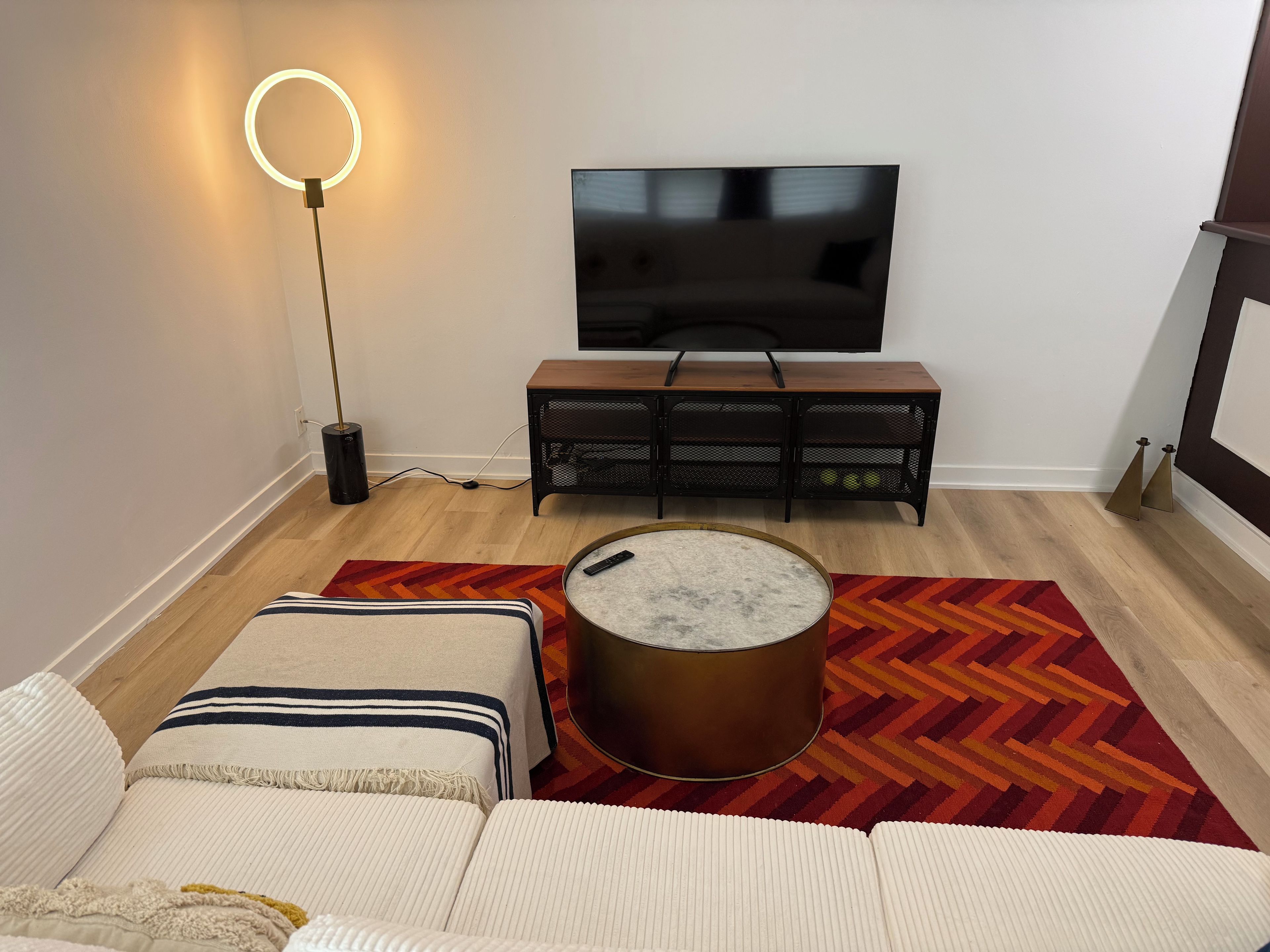 En stue med sofa, sofabord, fjernsyn på et stativ og en gulvlampe.