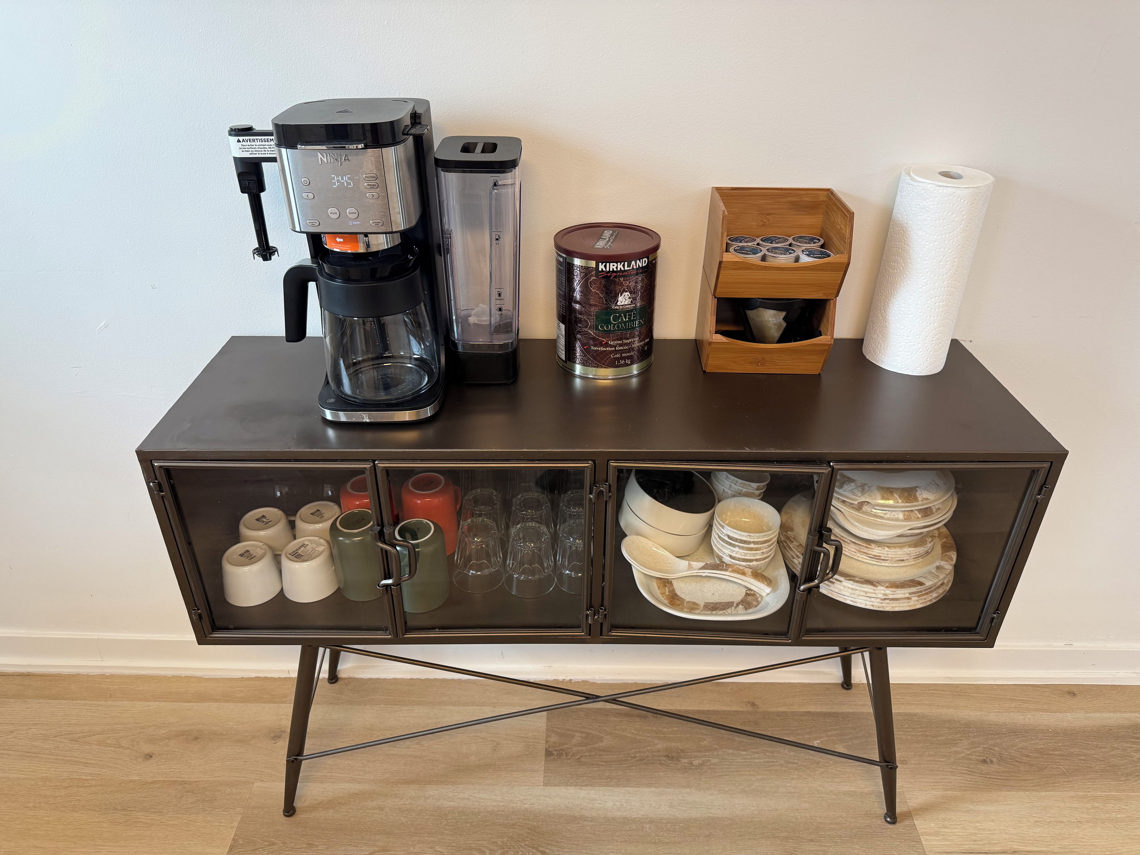 A coffee station with a coffee maker, a blender, a container of coffee, and a box of paper towels.