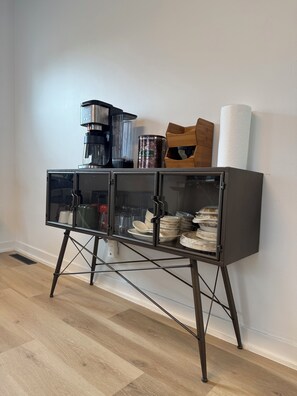 A kitchen area with a coffee maker, a canister, and a paper towel dispenser on a cabinet with glass doors.