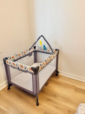 A baby playpen with a patterned fabric, a mesh top, and a small hanging toy.