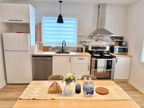 A modern kitchen with a built-in dishwasher, a stove, a microwave, and a window with blinds. - La Maison Country Route 132 | Charmant Bungalow (Sainte-Catherine)