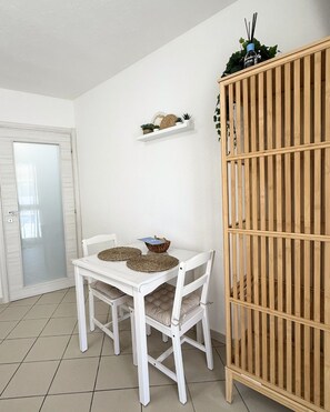 Un comedor con una mesa y sillas blancas, una repisa con objetos decorativos y un armario de madera.
