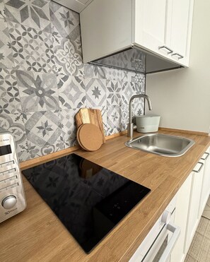 Una cocina moderna con tope de cocina por inducción negro, un lavamanos de acero inoxidable y azulejos decorativos en la respectiva pared.