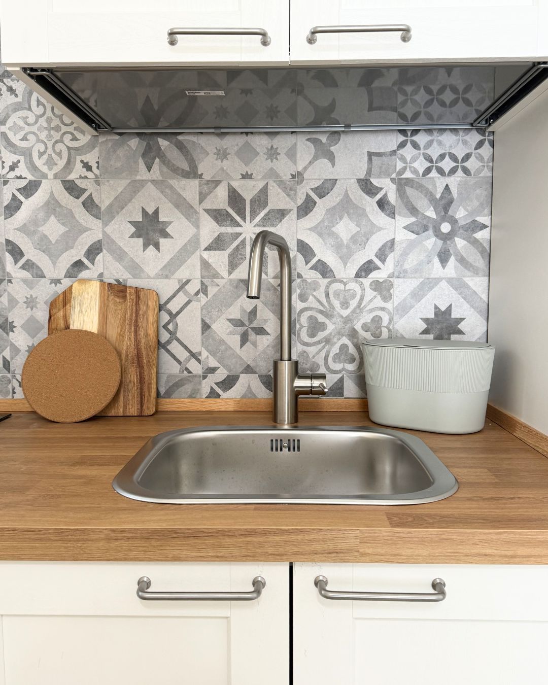 A kitchen with a stainless steel sink, patterned backsplash, and wooden countertop.