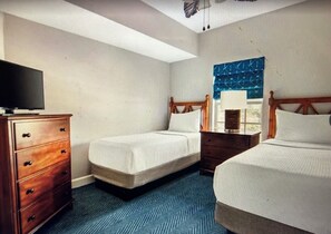 Hotellihuone, jossa on kaksi sänkyä, puinen lipasto, televisio ja kuviollinen matto.