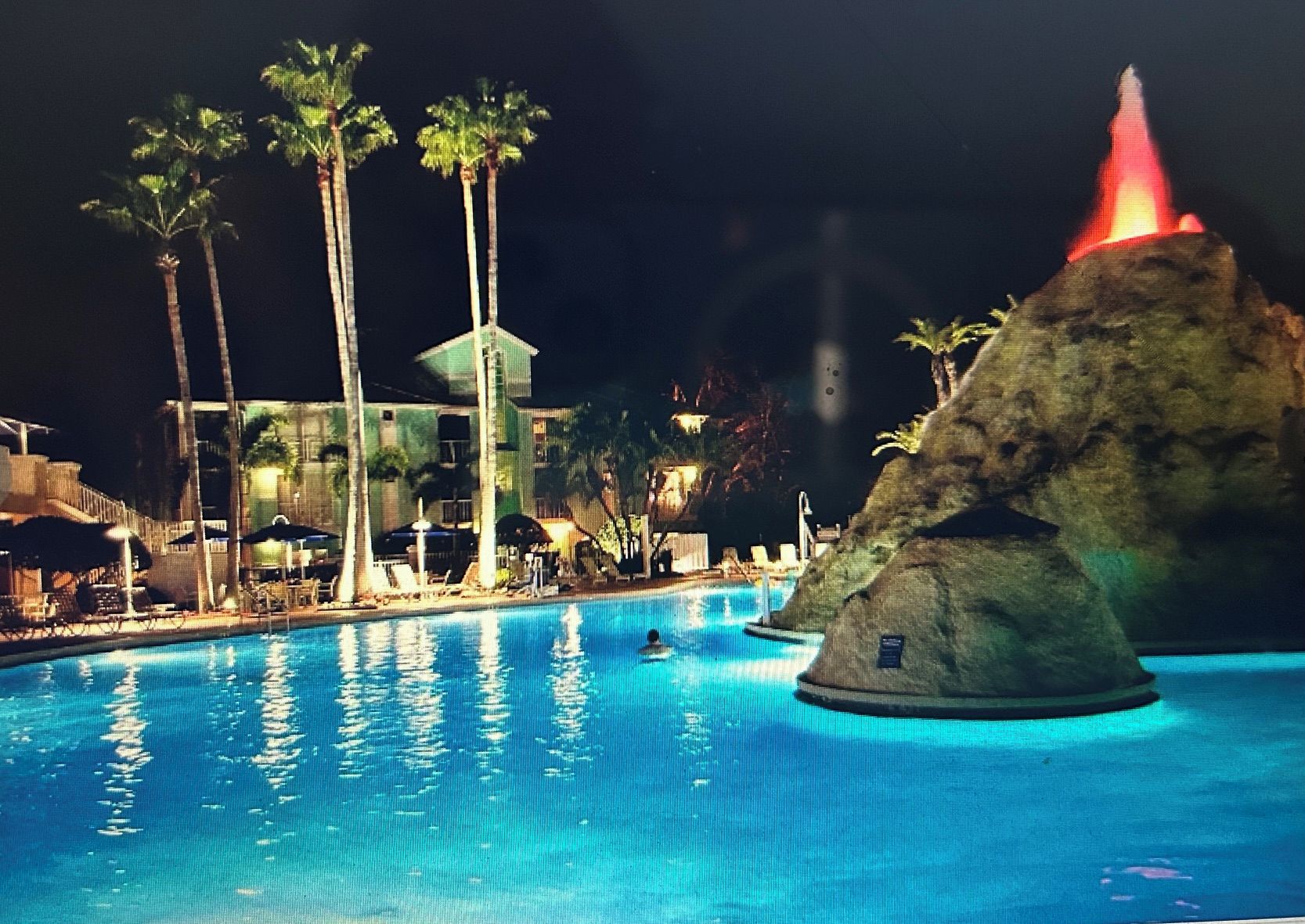 Piscina con palmeras y una formación rocosa con una luz roja.