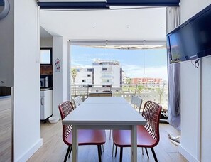 A modern dining area with a large table and red chairs, a kitchen with white cabinets, and a TV mounted on the wall. - Alpine Ski Apartment in Tignes for 4 (Agde)