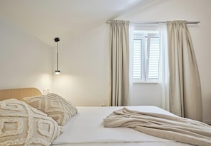A bedroom with a bed, a bedside lamp, a window with curtains, and a wall-mounted light fixture. - Hedera Estate, Hedera A18 (Dubrovnik)