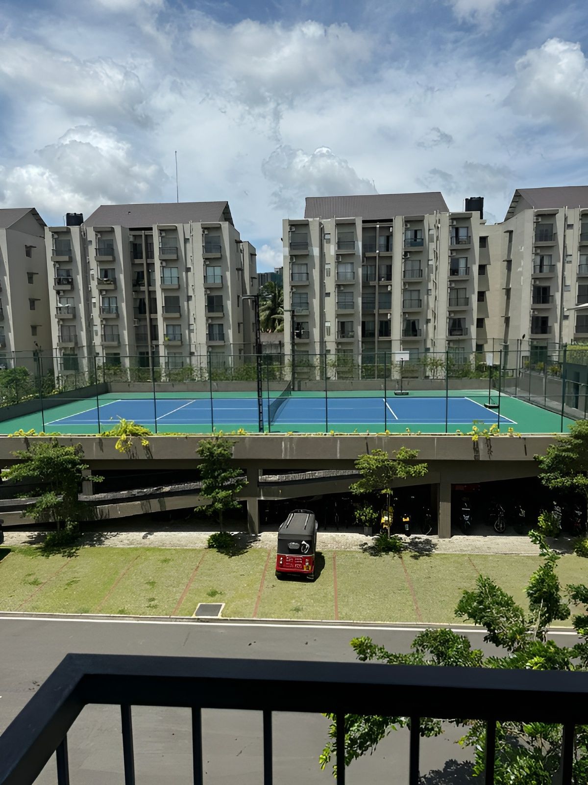 A residential building with multiple floors, a tennis court, and a parking area.