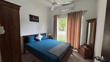 Quarto com cama, ventilador de teto, janela com cortinas, cômoda e espelho.
