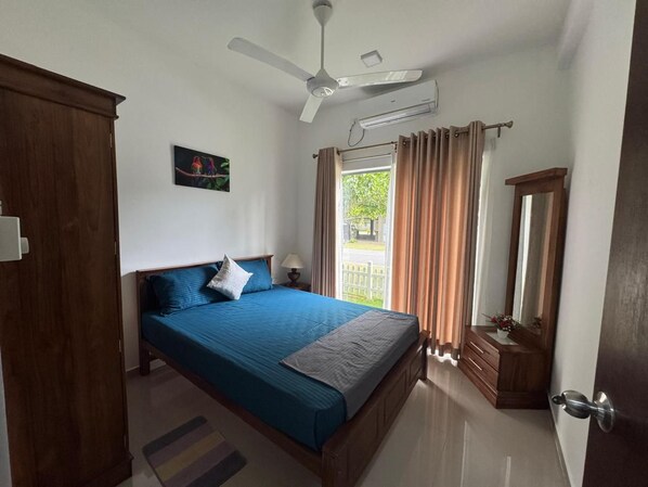 A bedroom with a bed, a ceiling fan, a window with curtains, a dresser, and a mirror.