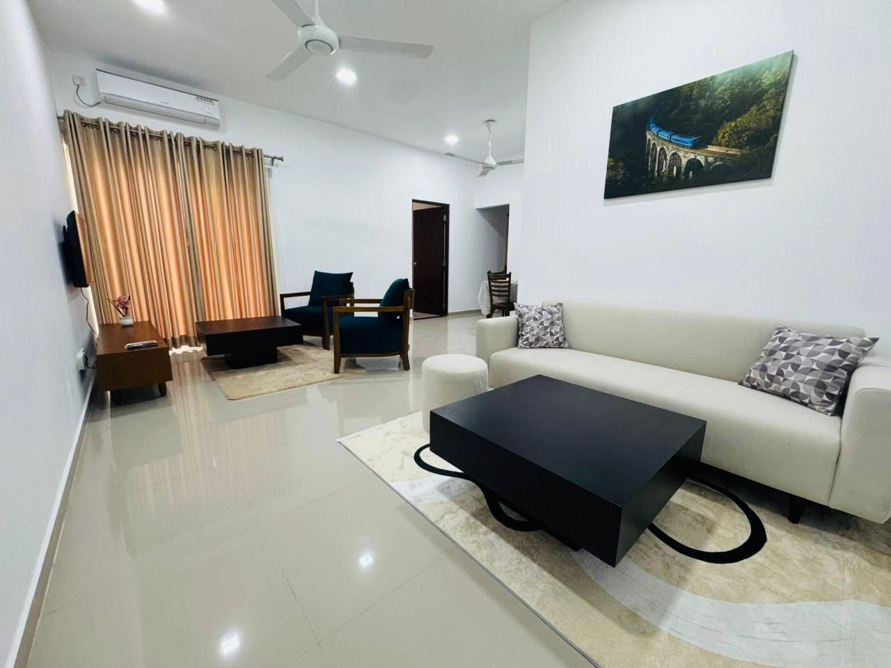 A modern living room with a sofa, coffee table, and chairs. There is a painting on the wall and an air conditioning unit on the ceiling.