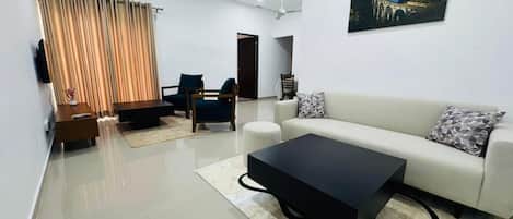 A modern living room with a sofa, coffee table, and chairs, an air conditioning unit, and a painting on the wall.