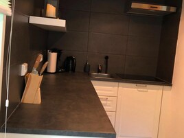 Una cocina moderna con encimera oscura, armarios blancos y un lavamanos de acero inoxidable.