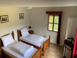 Una habitación con dos camas de madera, una mesita con lámpara, una ventana con vistas a zonas verdes y un aplique de techo.