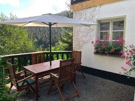 An outdoor patio with a table and chairs, a large umbrella, and a view of a forested area.