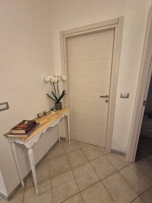 A hallway with a white door, a wooden console table with a plant and books, and a tiled floor. - Sos Ammntos (Memories) Vacation Home in Iglesias (Iglesias)