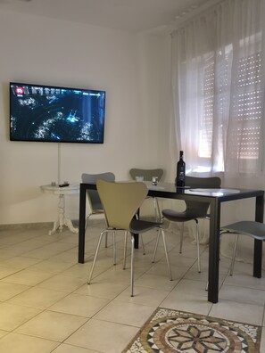 Ein Essbereich mit einem an der Wand befestigten Fernseher, einem Tisch mit Stühlen und einer Flasche auf dem Tisch.