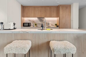 A modern kitchen with wooden cabinets, a marble countertop, a built-in microwave, and a stainless steel faucet. There are two fluffy stools at the bar. - Downtown Dubai 2BR near Burj Khalifa & Dubai Mall (Downtown Dubai)
