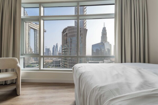 Ein Hotelzimmer mit großem Fenster und Blick auf die Stadt, ein Bett und ein Sessel.