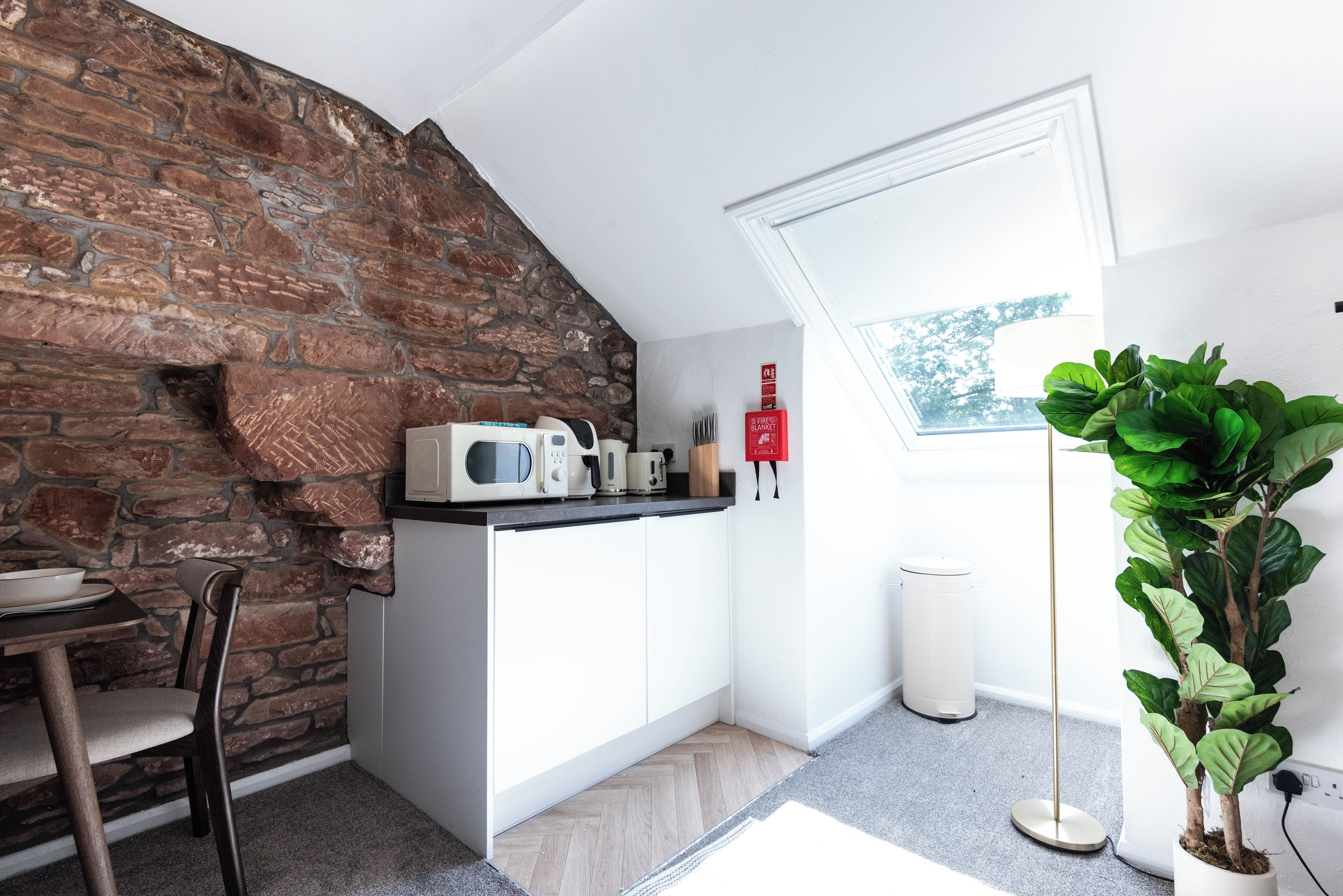 A compact kitchen with a stone wall, a microwave, a toaster, and a fire blanket on the counter.
