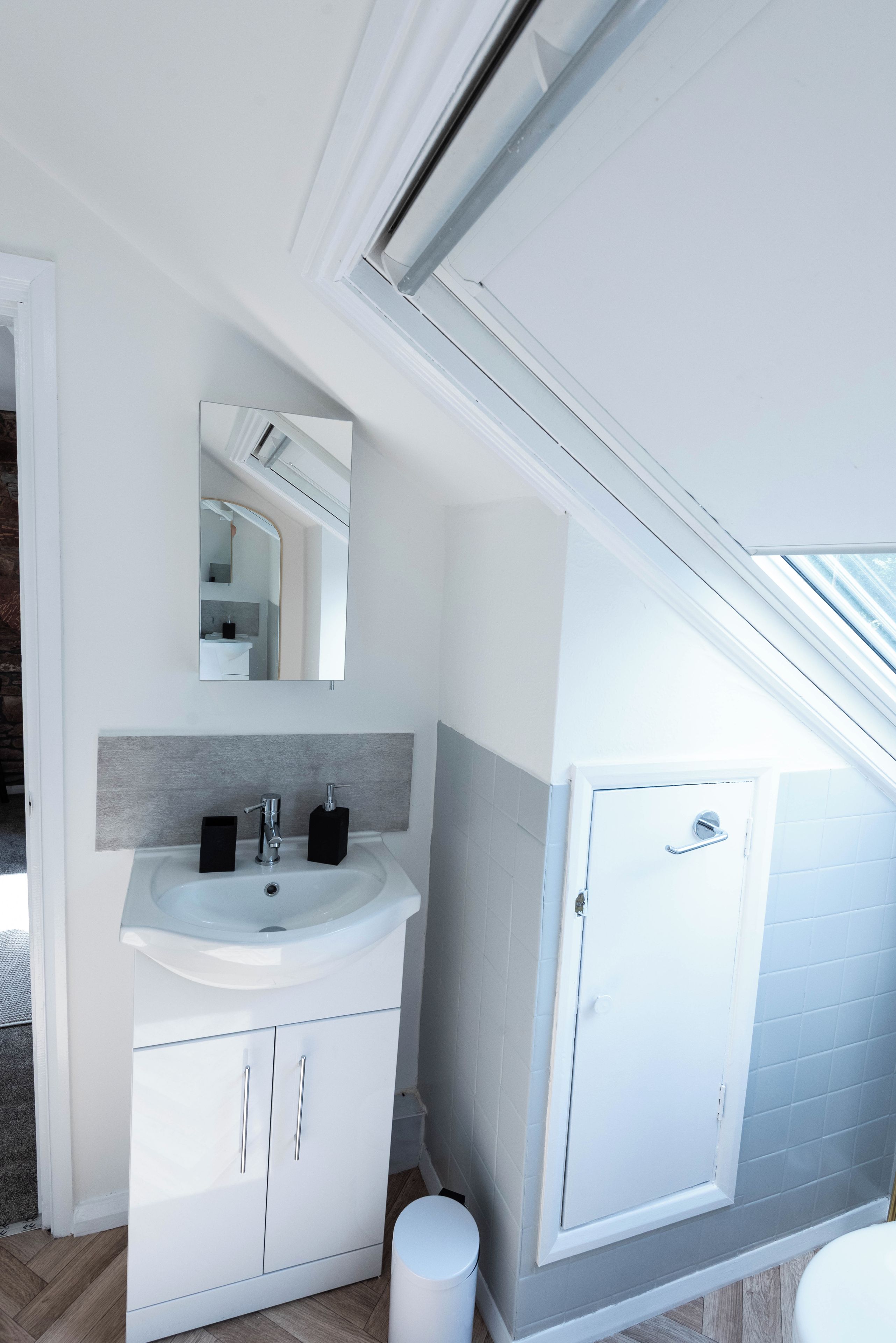 A modern bathroom with a skylight, white cabinetry, and a white toilet.