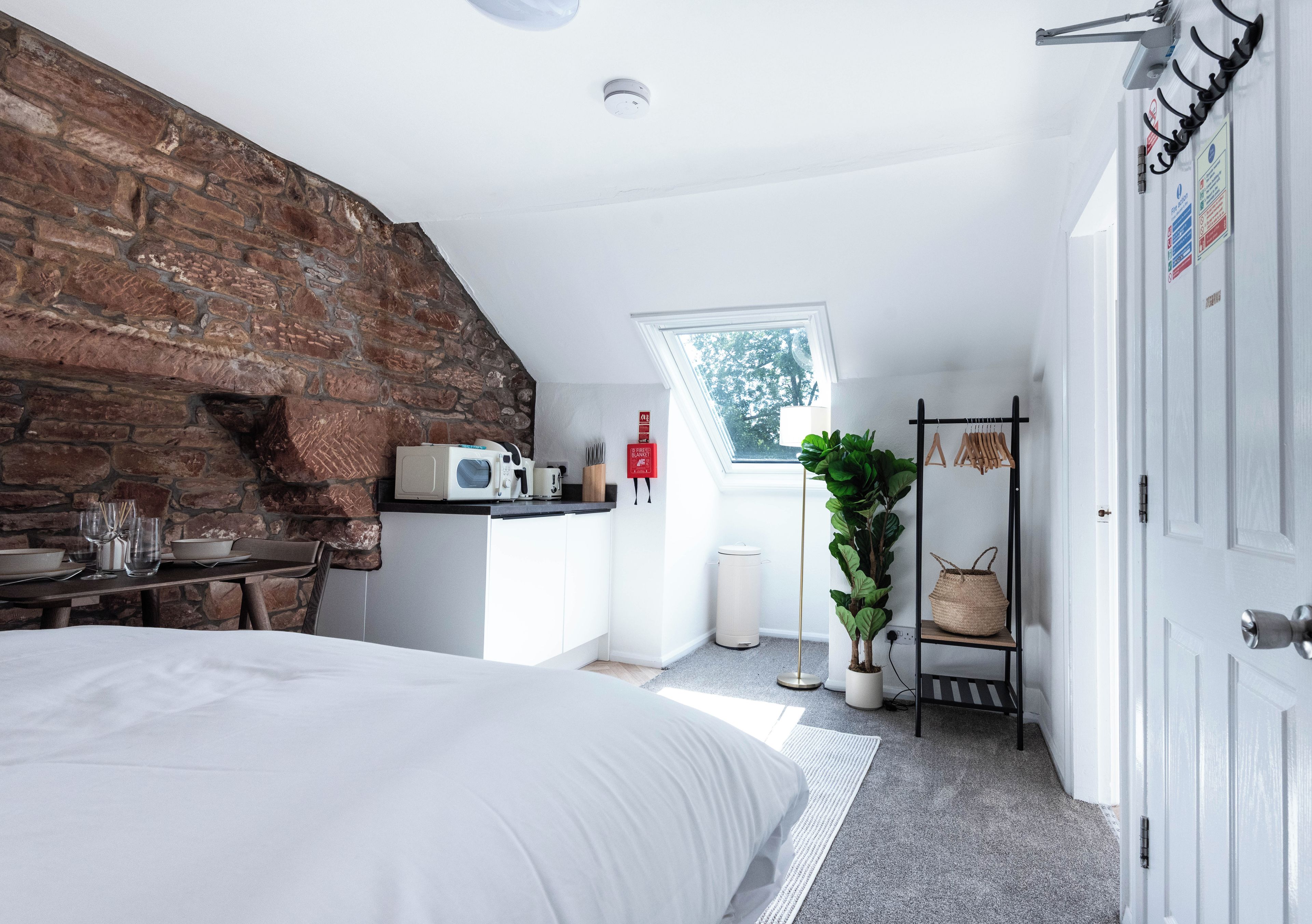 A bedroom with a large bed, a stone wall, a kitchenette, a window, and a plant.