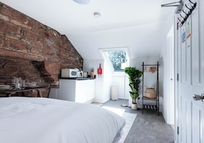 A bedroom with a large bed, a stone wall, a kitchenette, a window, and a plant. - The Stanley Arms Hotel by Guestz (Seascale)
